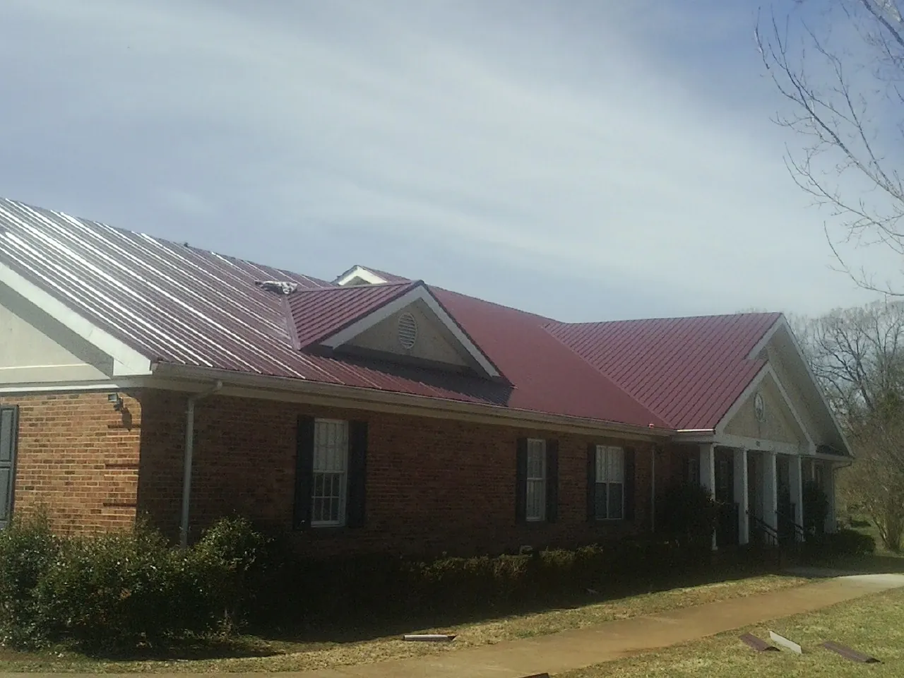 Red metal roof with gabled entries on a long brick building, from a Hail Damage Roof Repair job in Acton