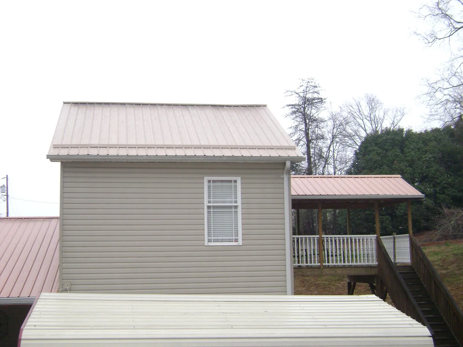 Tan metal roofs on a two story addition and attached porch, from a Roof Replacement job in Acton